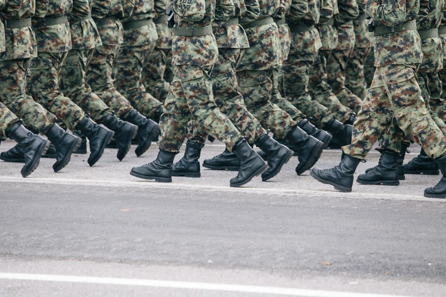 Service members marching in formation, seen from the waist down in camouflage uniforms and black boots.